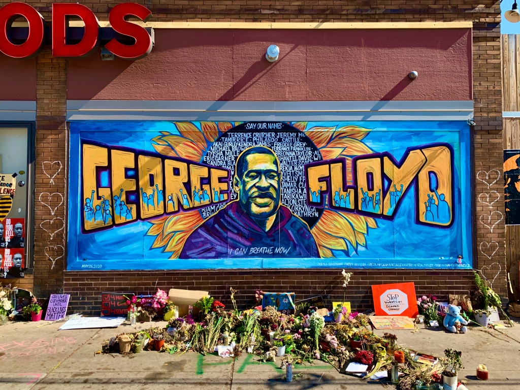 mural in Minneapolis of George Floyd with flowers and BLM signs on the sidewalk