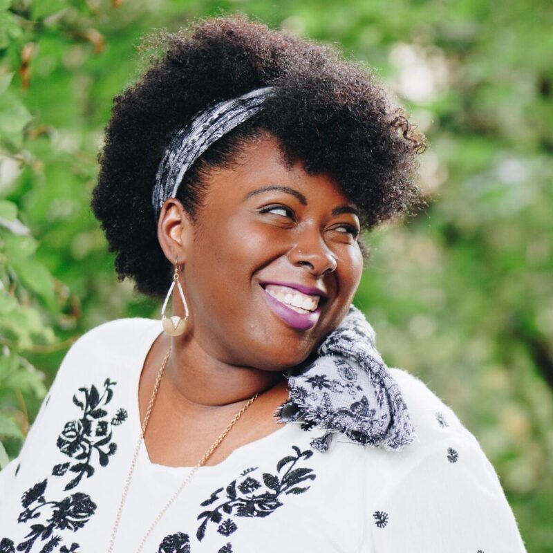 A fashionable woman with dark skin and natural hair smiling over her shoulder