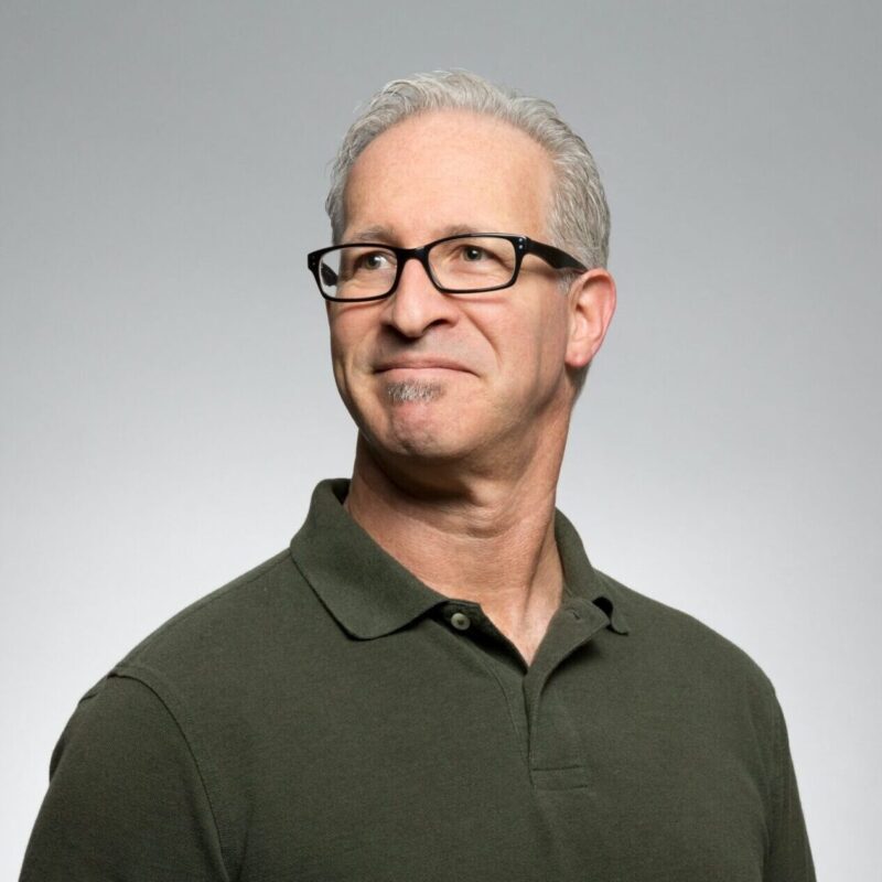 portrait of older man with gray hair and glasses giving a pensive smile