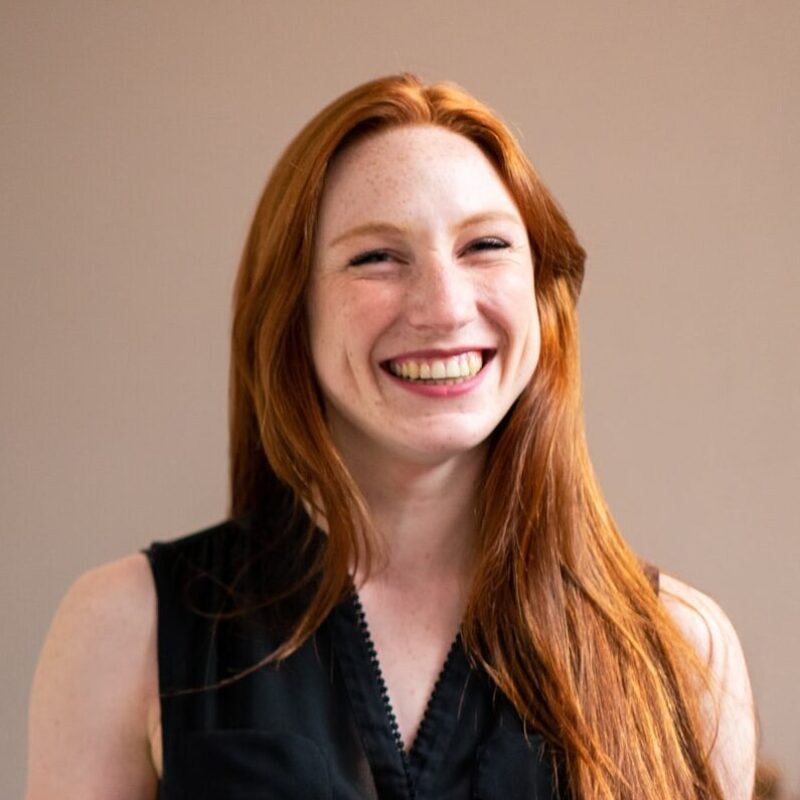 A woman with long red hair, fair skin, and a friendly smile