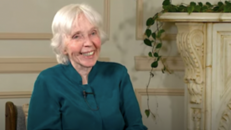Helen Palmer is an older woman with light skin and white hair. She is wearing a dark green shirt and smiling.
